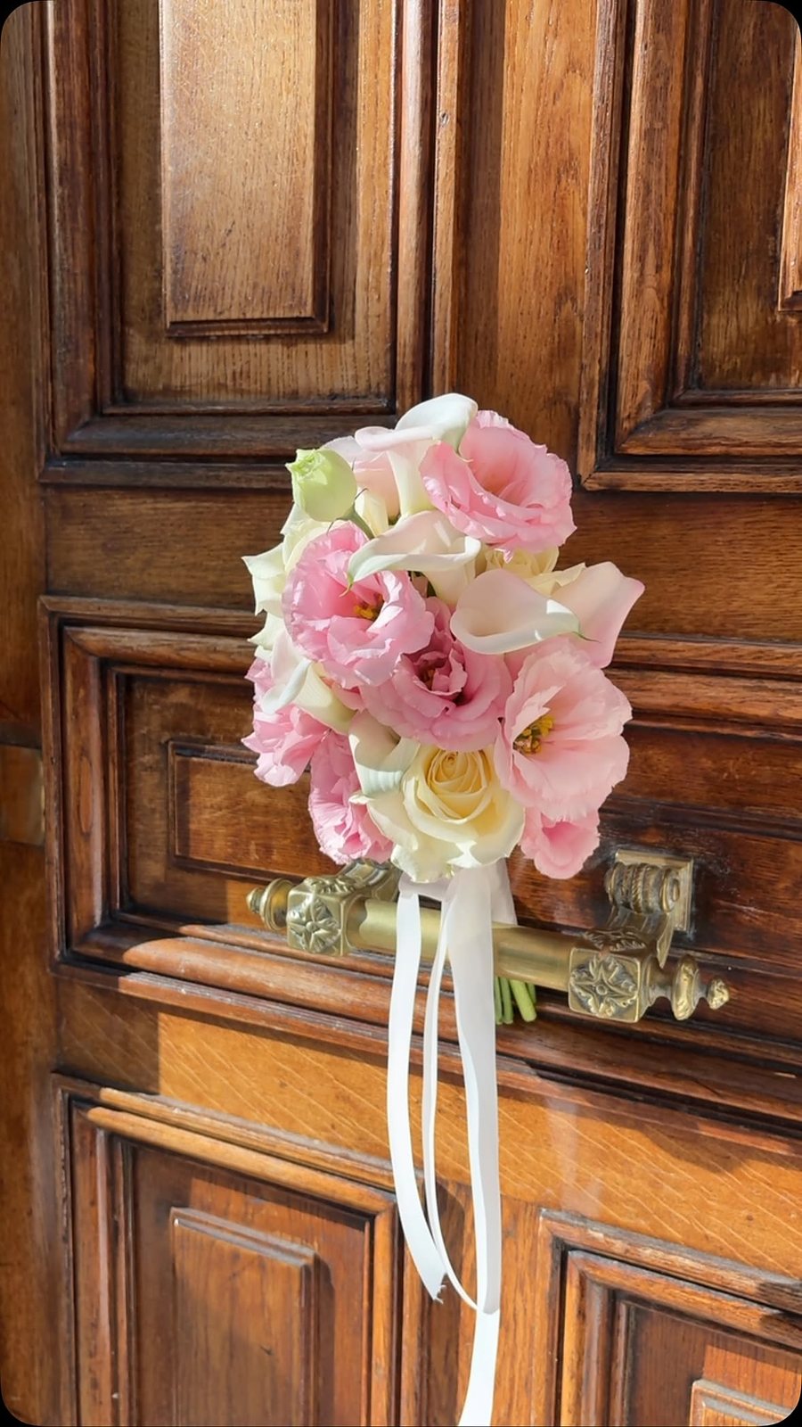 Bouquet de mariée rose et blanc, rubans tombants, devant une porte cochère