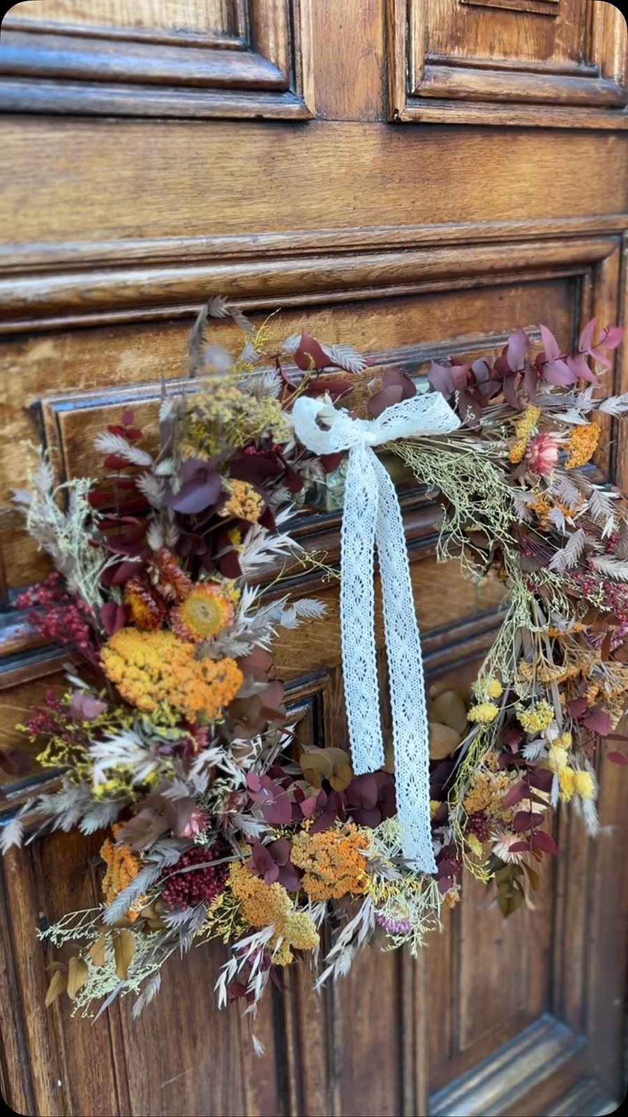 Couronne de fleurs séchées aux teintes d’automne accrochée à une porte